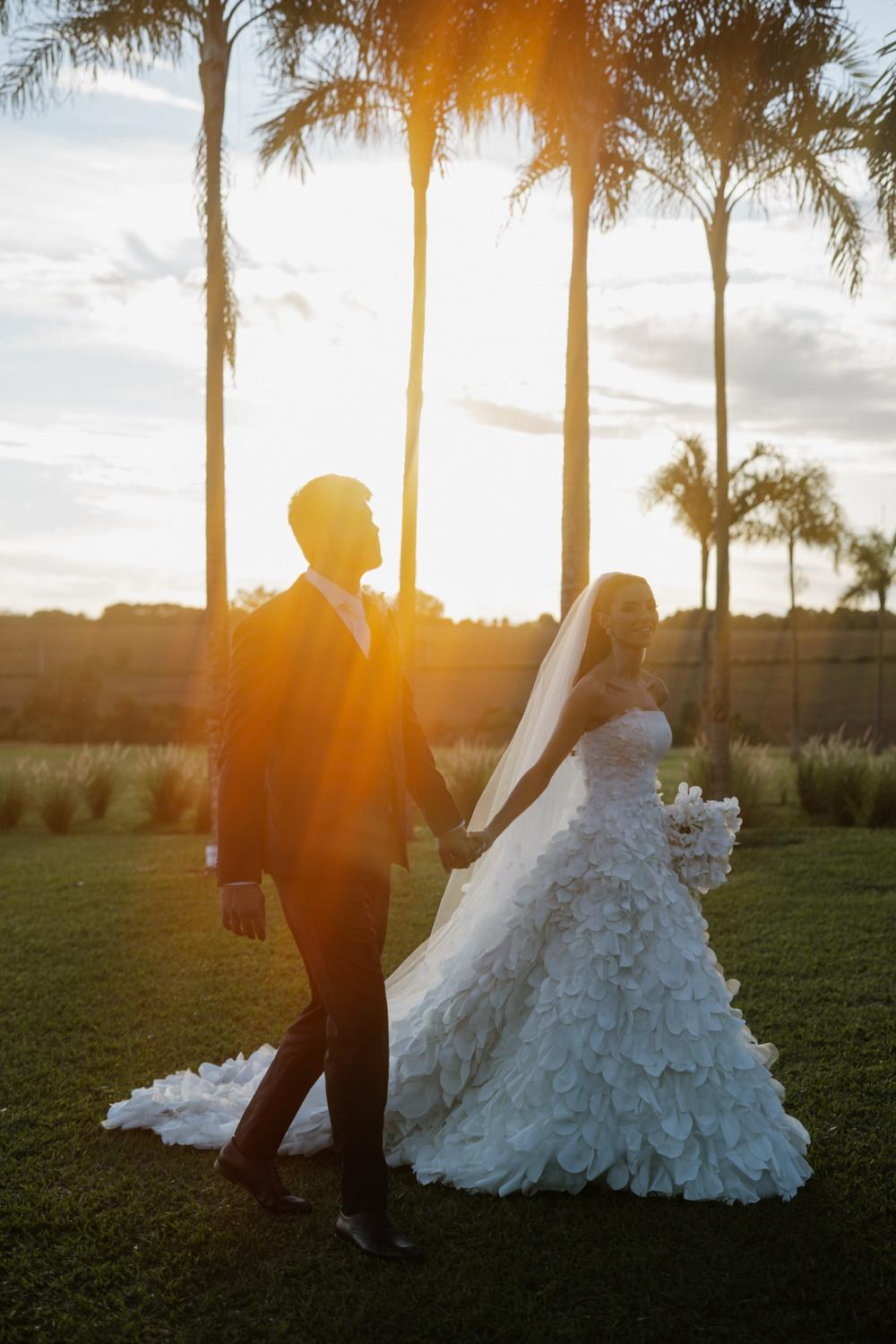 Novios de la mano al atardecer entre palmeras